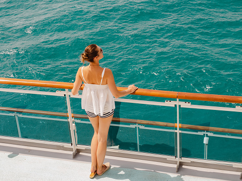 Beautiful woman standing on the empty deck of a cruise liner. Closeup, outdoor. Vacation and travel concept