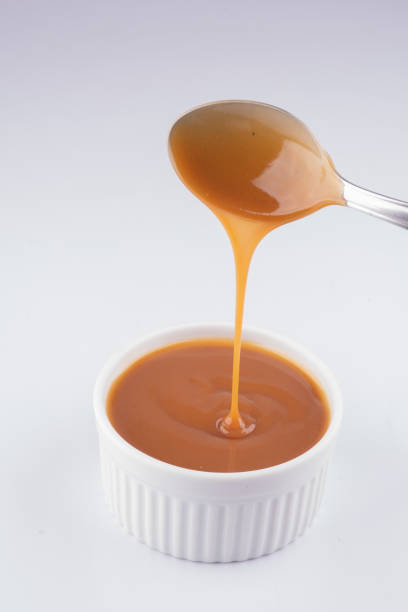 pouring dulce de leche with spoon into white pot isolated on white background pouring dulce de leche with spoon into white pot isolated on white background dulce de leche stock pictures, royalty-free photos & images