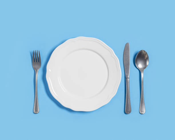 assiette blanche avec fourchette, couteau, cuillère sur fond bleu. assiette en céramique vide avec ensemble de couverts en métal, vue de dessus, maquette, espace de copie. vue d’en haut - fork table knife silverware spoon photos et images de collection