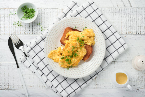 istock Scrambled Eggs. Fluffy and Buttery scrambled eggs on bread with microgreen radish and hollandaise sauce on white plate over white wooden background. Homemade breakfast or brunch meal. Top view. 1389486760