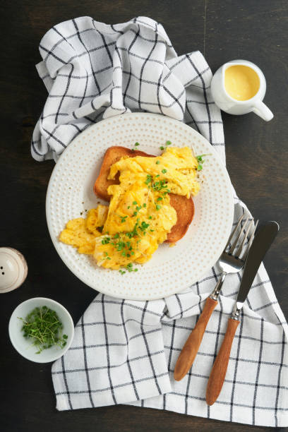 istock Scrambled Eggs. Fluffy and Buttery scrambled eggs on bread with microgreen radish and hollandaise sauce on white plate over dark old wooden background. Homemade breakfast or brunch meal. Top view. 1389486808