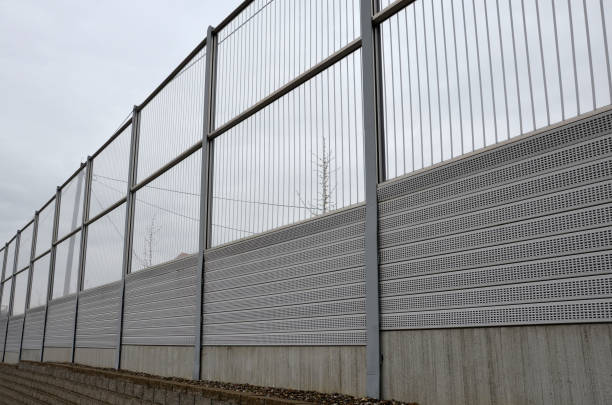 striped glass noise barrier made of metal perforated sheet metal slats. gray and silver protective fencing separates housing from a busy noisy road. the porous material shatters tire noise well. absorptive, absorbing, decibel, diffusion barrera contra el ruido de vidrio rayado hecha de listones de chapa perforada de metal. las cercas protectoras grises y plateadas separan la vivienda de una carretera ruidosa y concurrida. el material poroso rompe bien el ruido de los neumáticos.
