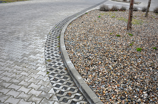 newly established street in the city, the longitudinal car park is made of perforated concrete infiltration tiles on the side of the road at the curb. slope stabilization using a terraced palisade, shattering