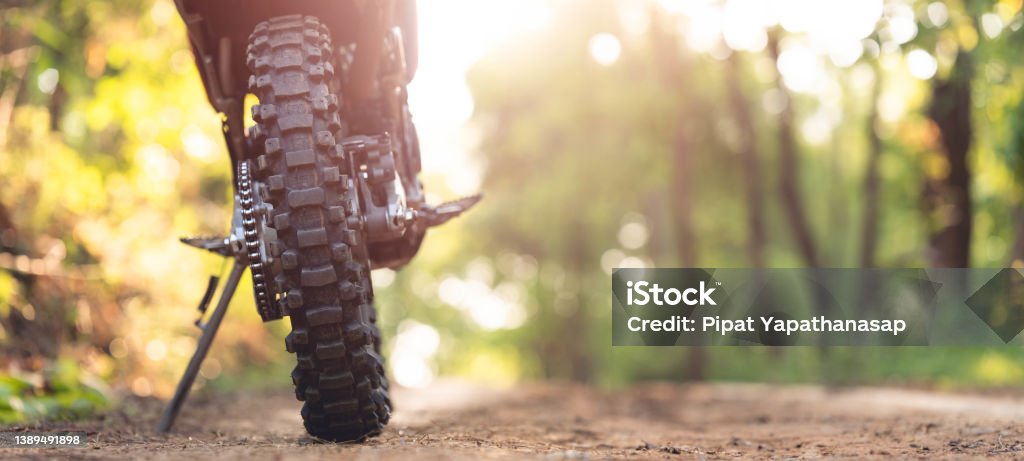 Part of a motocross wheel on a mound, with sunrise copyspace for your individual text. A part of a dirt road dirt bike in the forest Motocross Stock Photo