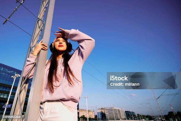 A Girl With Headphones On Metal Construction On A Railroad Station Is Looking Towards The Sun Stock Photo - Download Image Now