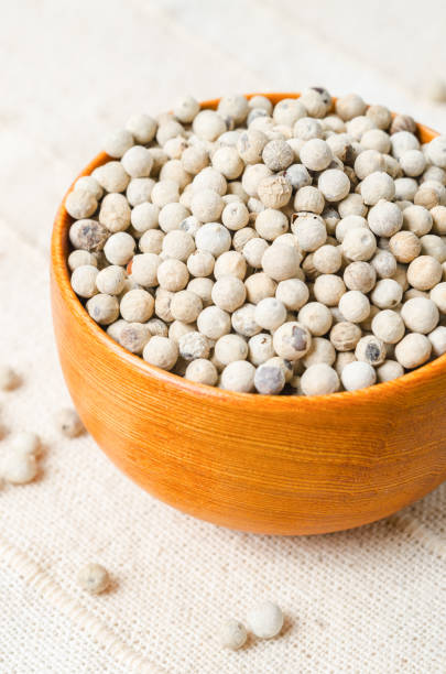 istock White pepper seeds (peppercorn) in wooden bowl on tablecloth background. 1389492334