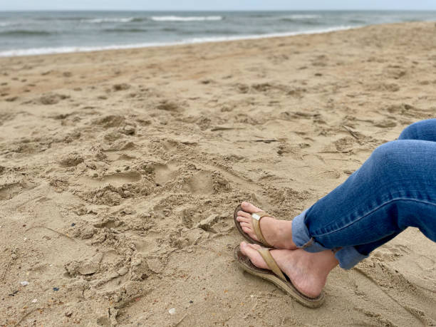 Feet & Legs of a Woman Relaxing at a Beach A woman wearing flip-flops on her feet relaxes at the beach along the Atlantic Ocean in the Outer Banks of North Carolina on a cool afternoon. flip flop sandal beach isolated stock pictures, royalty-free photos & images