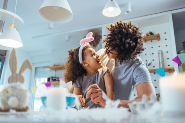 istock Smiling man painting easter eggs. Little girl painting easter egg using a paint brush sitting with her father. 1389494154