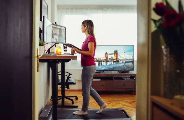 Standing desk home office with under desk treadmill Woman working from home at standing desk is walking on under desk treadmill standing desk photos stock pictures, royalty-free photos & images