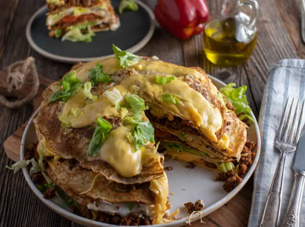 Delicious savory pie made with pancakes filled with ground beef, beans, sour cream, tomatoes, lettuce and cheese. Served on rustic and wooden table background. Ready to eat