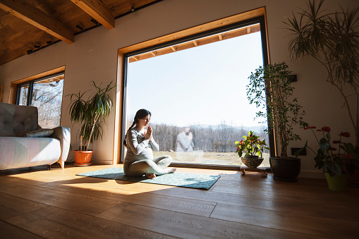 Young pregnant woman in lotus position meditating at home.