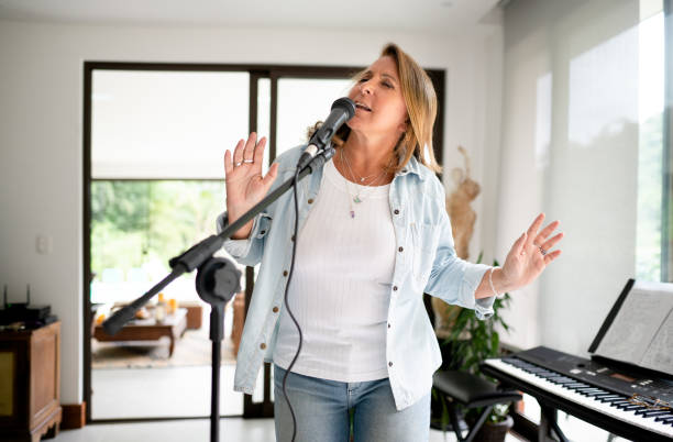 Mature woman standing with her eyes closed and singing into a microphone during a rehearsal in her home recording studio