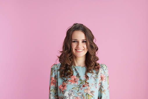 Portrait of happy young woman in floral dress against pink background.