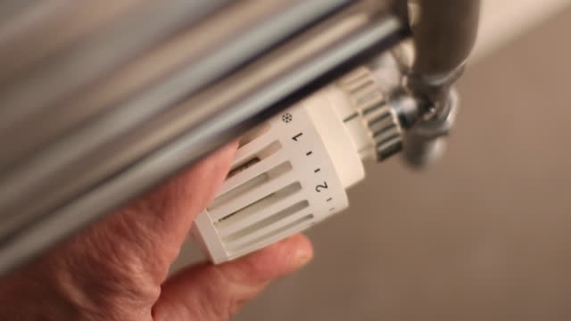 Radiator thermostatic valve adjustment, zoom in. Male hand turning the heat down.