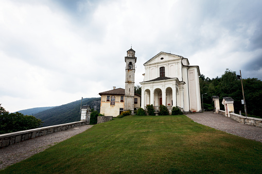 Grassy land leading towards Madonna del Sasso sanctuary against cloudy sky in Piedmont, Italy