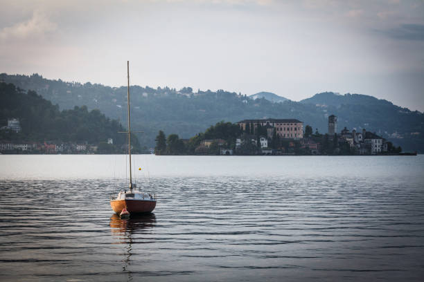 Small sailboat moored on Lake Orta against mountains and cloudy sky during sunset at Orta San Giulio, Italy