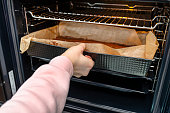 The woman puts the baking tray with the raw dough for the pie in the oven.