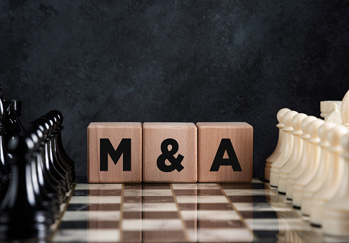 Chessboard with chess pieces and wooden blocks with the word mergers and acquisitions (M&A). Business merger and acquisition strategy concept.