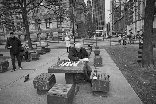 Toronto Ontario, Canada- April 3rd, 2022: A man reading a book while his chess pieces are set up and ready to be played.