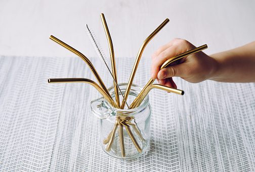 Child hand take golden metal drinking straw in home kitchen. Sustainable lifestyle concept.
