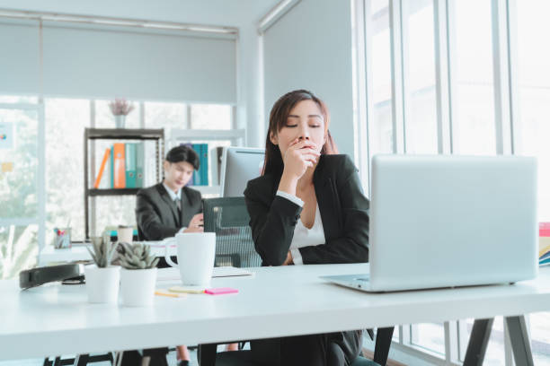 Sleepy female officer is yawning in afternoon office after tired and boredom at workplace. stock photo