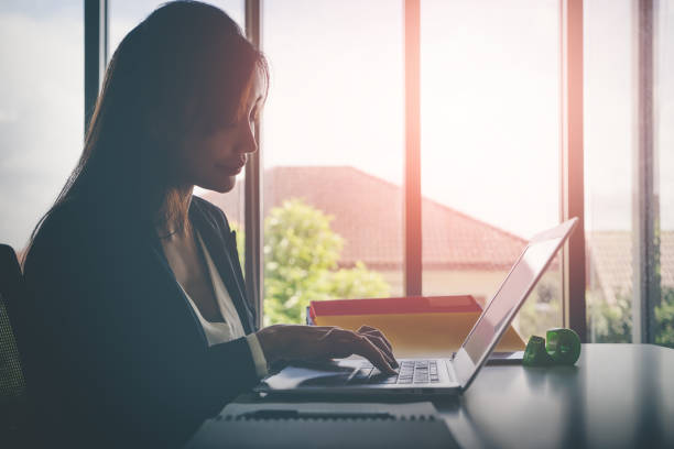 istock Asian woman working on laptop computer alone, Silhouette sunlight tone. 1389516482