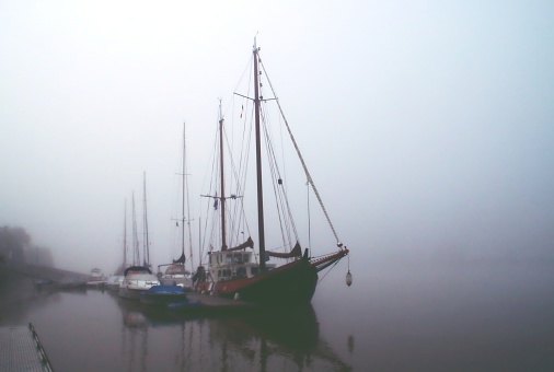 Tapia de Casariego harbor in thick fog, touristic location. Rows of moored fishing boats defocused, stone dock, lighthouse .