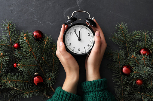 Woman with alarm clock near Christmas decor on black slate background, top view. New Year countdown