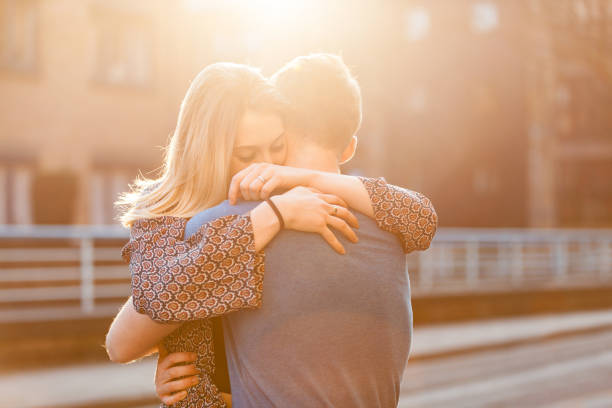 A happy couple enjoying a warm sunset together. The man is gently leaning in, smiling, while the woman laughs with joy. The golden light of the sunset highlights their faces, creating a beautiful and romantic moment. They look carefree and deeply connected, sharing a special time outdoors.