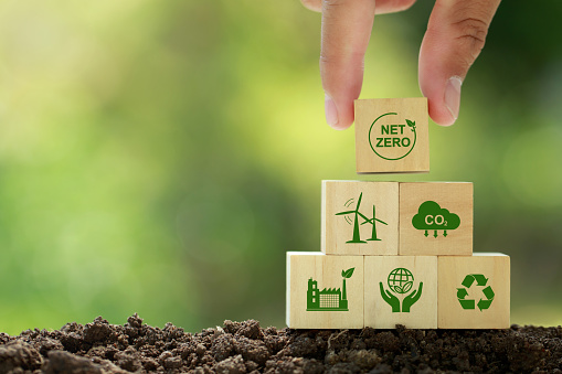 Net zero and carbon neutral concept. Hand puts wooden cubes with netzero icons - renewable energy, co2 emissions reduction, green production, waste recycling.in green background