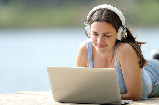Mujer con auriculares usando computadora portátil acostada en el muelle photo