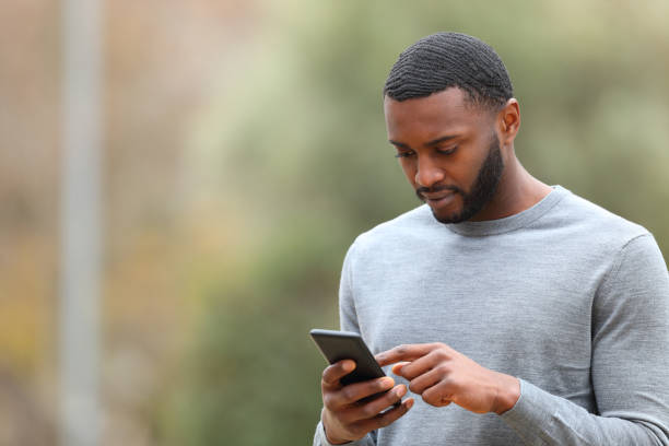 istock Man with black skin using cell phone walking in a park 1389525624
