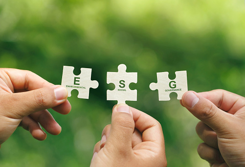 ESG concept of environmental, social, and governance.Hand of people holding a piece of jigsaw puzzle with the word ESG to represent collaboration involvement in solving environmental, social