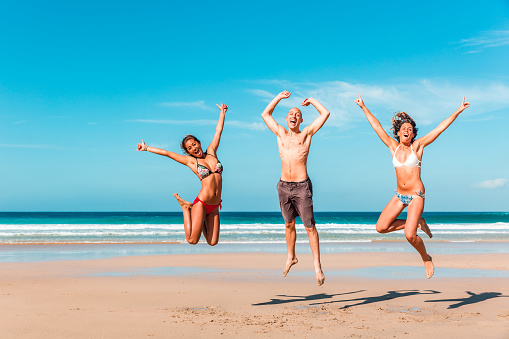 Happy multiracial friends jumping and celebrating at seaside - Multiethnic people having fun together in sunny Fuerteventura - Man and women at beach enjoying time together