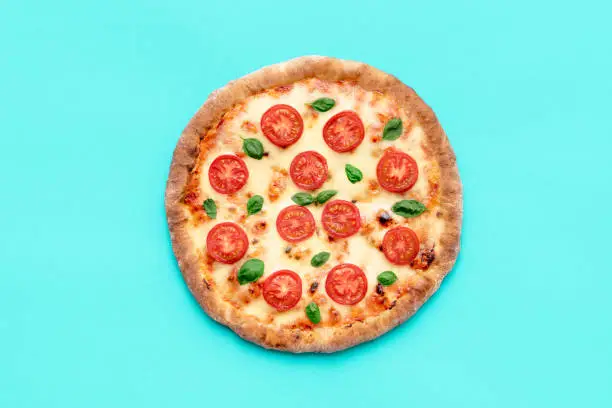 Top view with a homemade pizza on a blue table. Ready to eat delicious vegetarian pizza made with tomato, mozzarella, and basil.