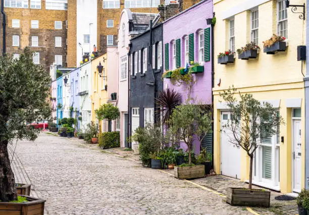 A long row of pastel coloured mews houses on a cobbled street in Kensington, :London.