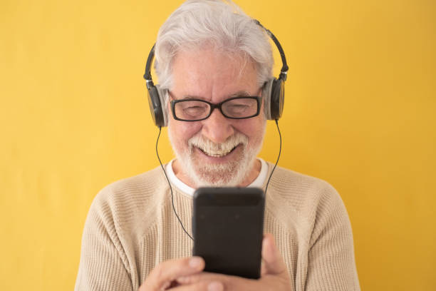 istock Cheerful white-haired senior man wearing black headphones while using mobile phone listening music or watching video. Attractive elderly grandfather enjoying tech and social 1389527680