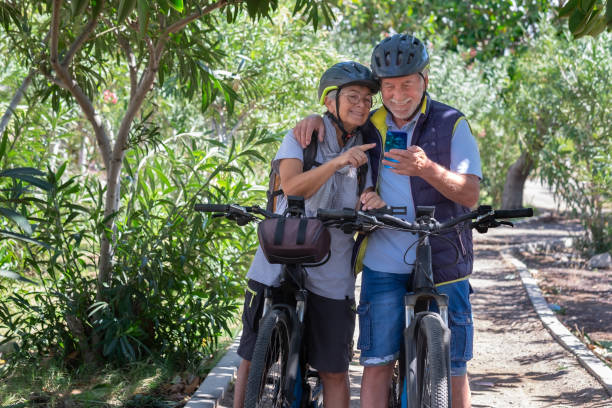 istock Active caucasian senior couple with electrobikes standing outdoors in the park video calling by cellphone. Two smiling elderly people wearing helmet running in nature enjoying healthy lifestyle 1389529866