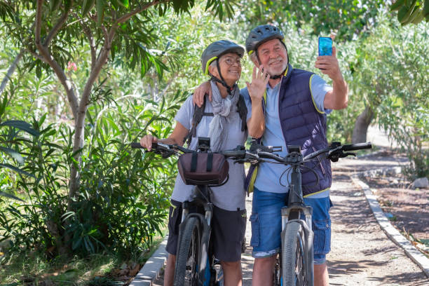istock Active caucasian senior couple with electrobikes standing outdoors in the park video calling by cellphone. Two smiling elderly people wearing helmet running in nature enjoying healthy lifestyle 1389530076