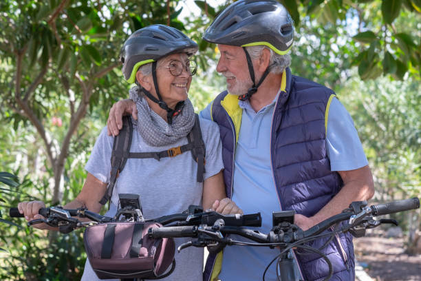 istock Active senior caucasian couple with electrobikes standing outdoors in the park hugging. Two happy elderly people looking in the eyes enjoying nature and healthy lifestyle 1389530255