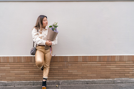 A full length portrait of a beautiful woman holding flowers.