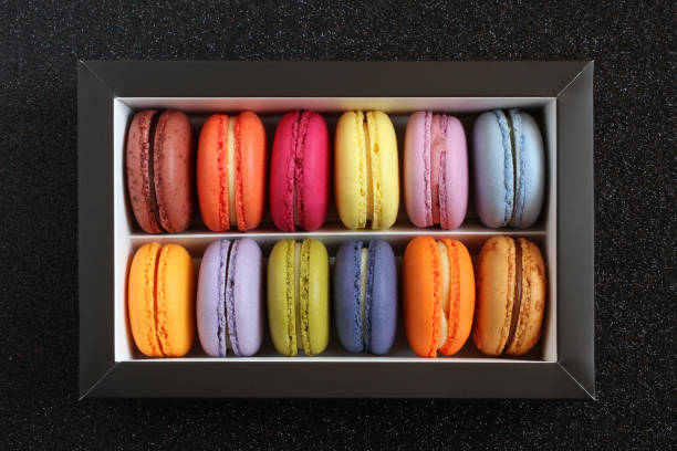 istock Multicolored macarons in a cardboard box without a lid on a black glitter surface. View from above. Closeup 1389534548