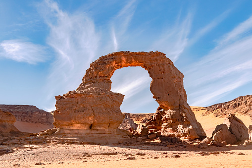 Tassili n'Ajjer national park, Djanet, Illizi. Blue cloudy sky with wonderful colors of the naturally sculpted arch shaped stone with the amazing natural draw of the African continent inside.