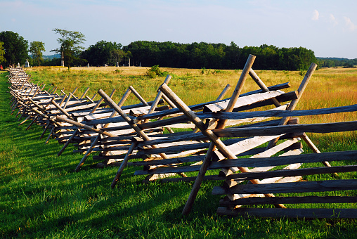 A wood split rail fence cuts through a field and meadow at Gettysburg National Battlefield.