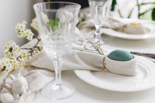 istock Easter egg in bunny napkin on plate with cutlery, bunny, spring flowers on rustic white table. Stylish elegant Easter brunch table setting. Modern table arrangement and eco decoration 1389542802