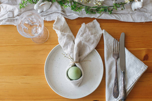 istock Easter egg in bunny napkin on plate with cutlery, bunny, spring flowers and rustic cloth on wooden table. Top view. Stylish Easter brunch table setting. Happy Easter! 1389542902