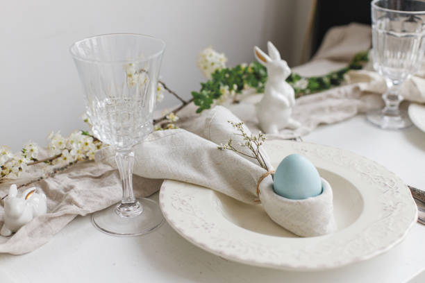 istock Easter egg in bunny napkin on plate with cutlery, bunny, spring flowers on rustic white table. Stylish elegant Easter brunch table setting. Modern table arrangement and eco decoration 1389543053