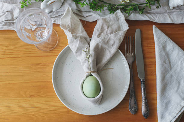 istock Happy Easter! Easter egg in bunny napkin on plate with cutlery, bunny, spring flowers and rustic cloth on wooden table. Top view. Stylish Easter brunch table setting. 1389543178