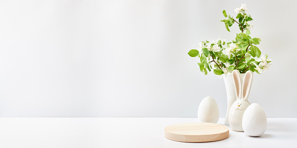 Empty round wooden podium for product presentation. Spring flowers in a vase, easter eggs on a light background. Mockup concept with copy space