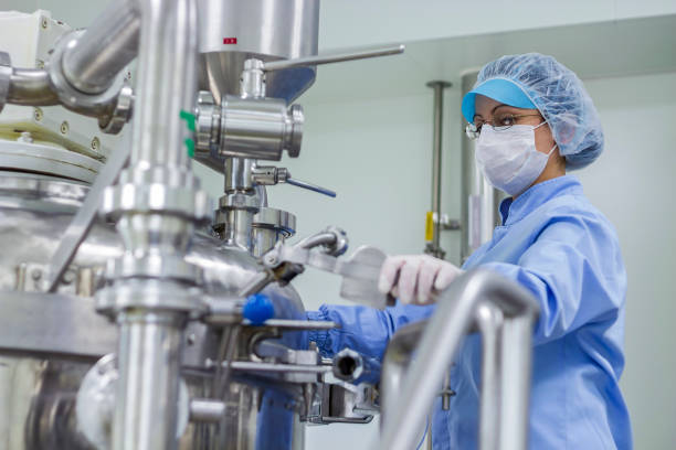 Pharmaceutical Industry Worker At Work In Sterile Environment Preparing Machine For Work In Pharmaceutical Factory. Female Worker Wearing Protective Clothing In Pharmaceutical Plant. drug manufacturing stock pictures, royalty-free photos & images